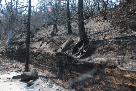 Image of a large cast iron flywheel resting on burned-out hillside